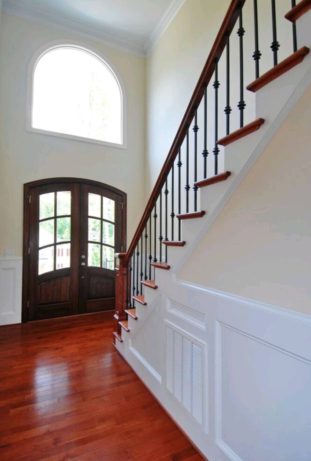 Bright foyer with curved wooden staircase, red wood floor, and tall arched window above double front doors
