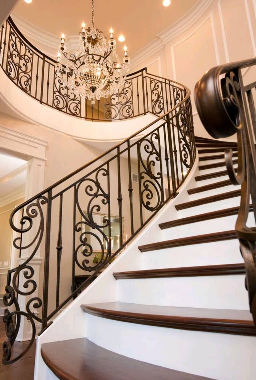 Elegant curved staircase with ornate iron railing and chandelier in a bright foyer