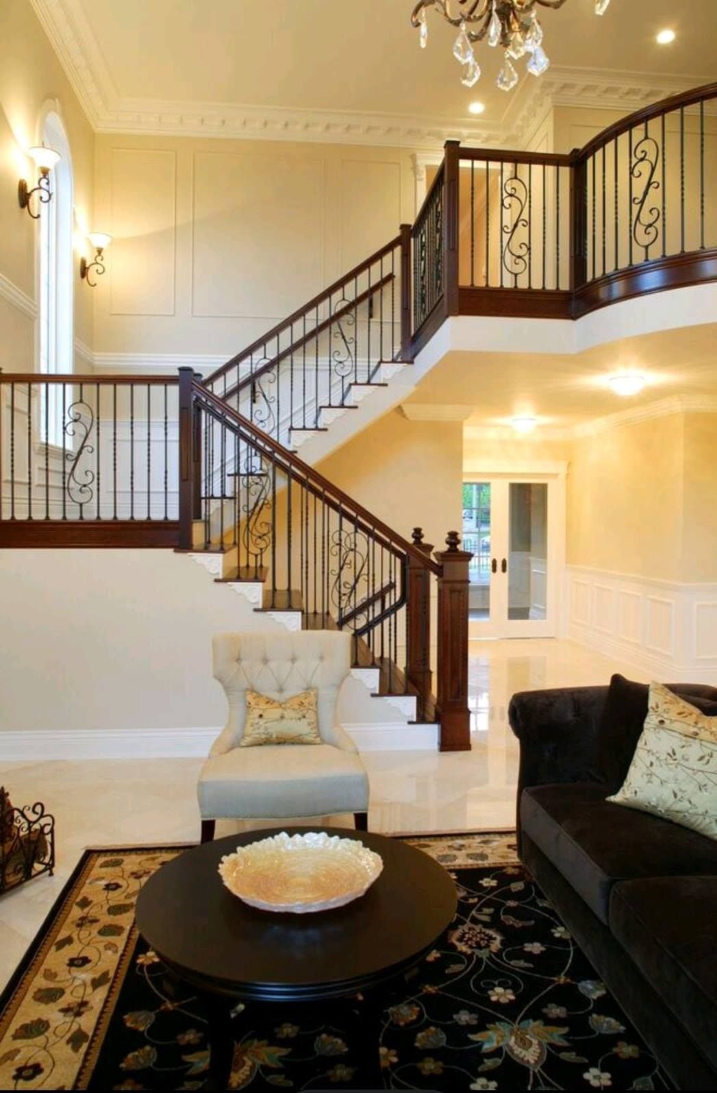 Elegant foyer with curved staircase, chandelier, and dark wood railing in a warmly lit home