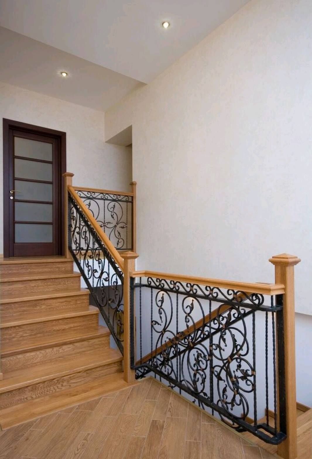 Interior staircase with wood steps, ornate black railing, and beige walls leading to an upper landing