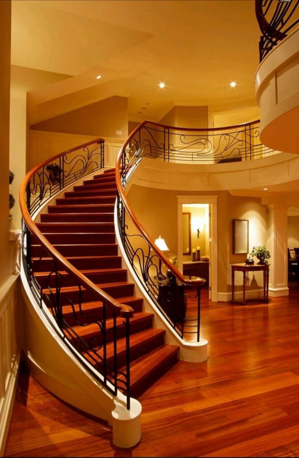 Curved wooden staircase with ornate railings in a warmly lit luxury interior lobby