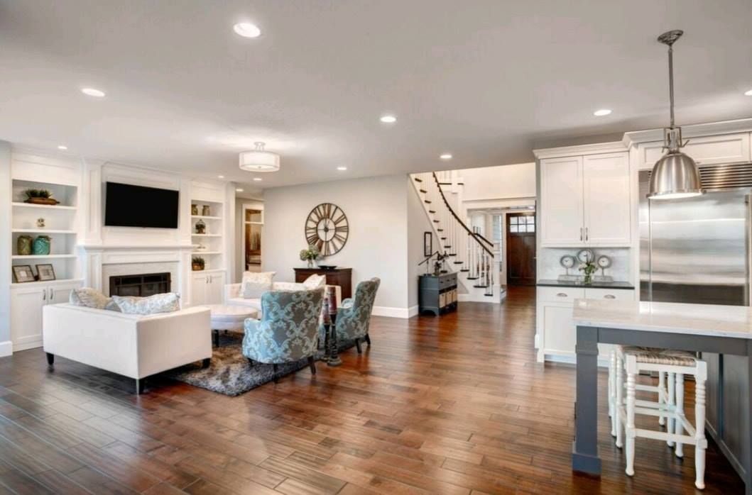 Open-concept living room and kitchen with hardwood floors, white furniture, island, and staircase.