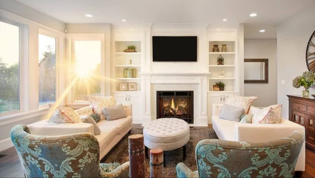 Bright living room with two sofas, patterned chairs, ottoman, and fireplace beneath a wall-mounted TV