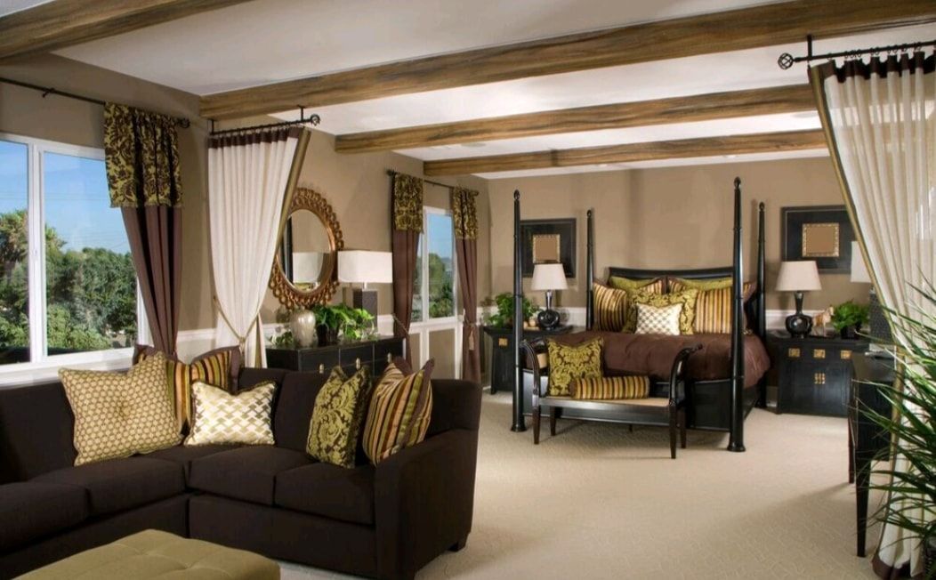 Elegant living room with dark sofas, patterned pillows, cream curtains, and wood beams overlooking greenery