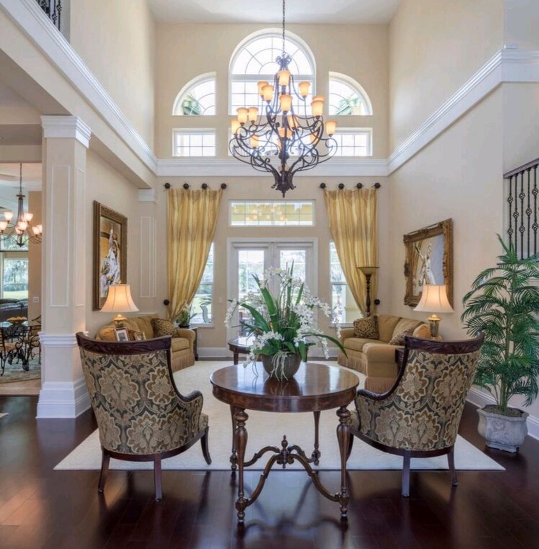 Elegant foyer with chandelier, arched windows, round table, and patterned armchairs