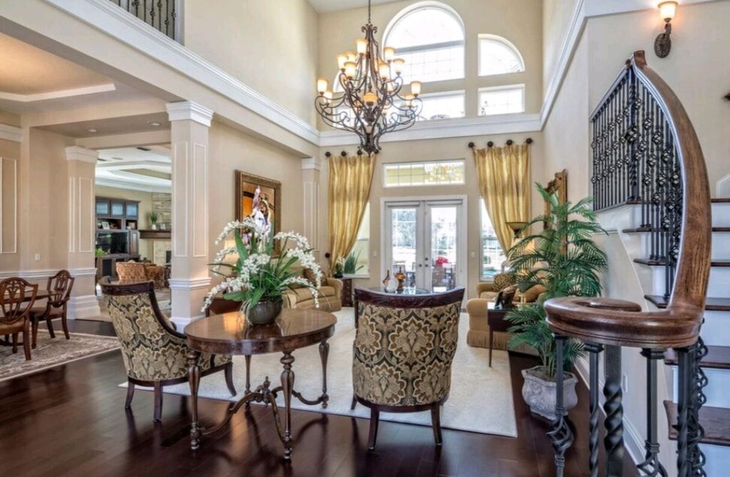 Elegant foyer with chandelier, arched window, staircase, and ornate chairs around a table