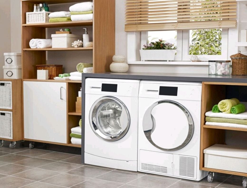 Bright laundry room with front-load washer and dryer, wooden shelves, and a window with blinds
