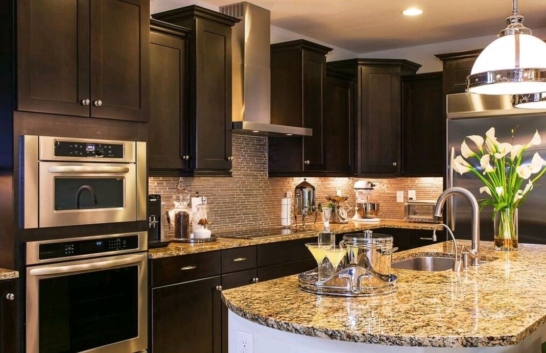 Modern kitchen with dark cabinets, granite island, built-in oven, and vase of white flowers