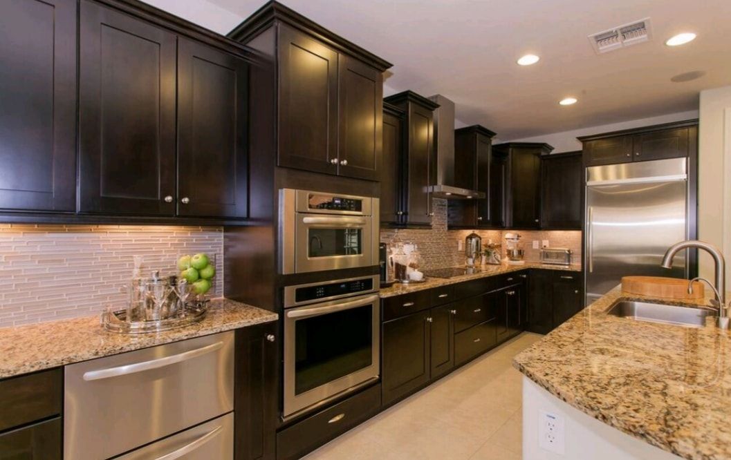 Modern kitchen with dark cabinets, granite countertops, stainless steel appliances, and an island sink