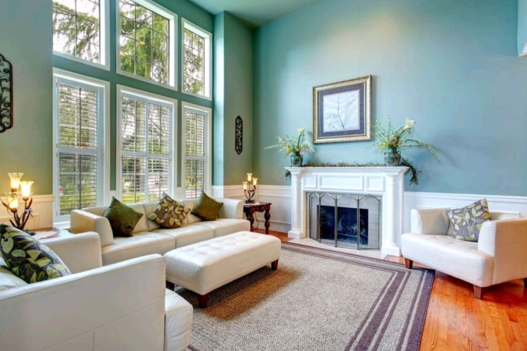 Bright living room with large windows, white furniture, teal walls, and a fireplace