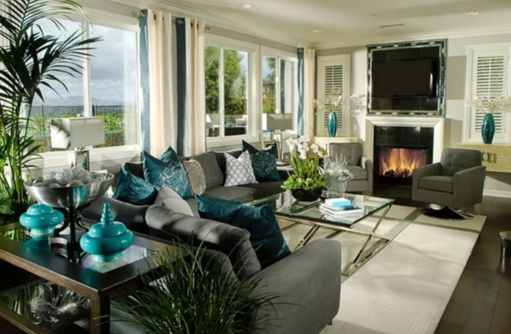 Bright living room with teal accents, beige sofas, large windows, and a fireplace with TV above.