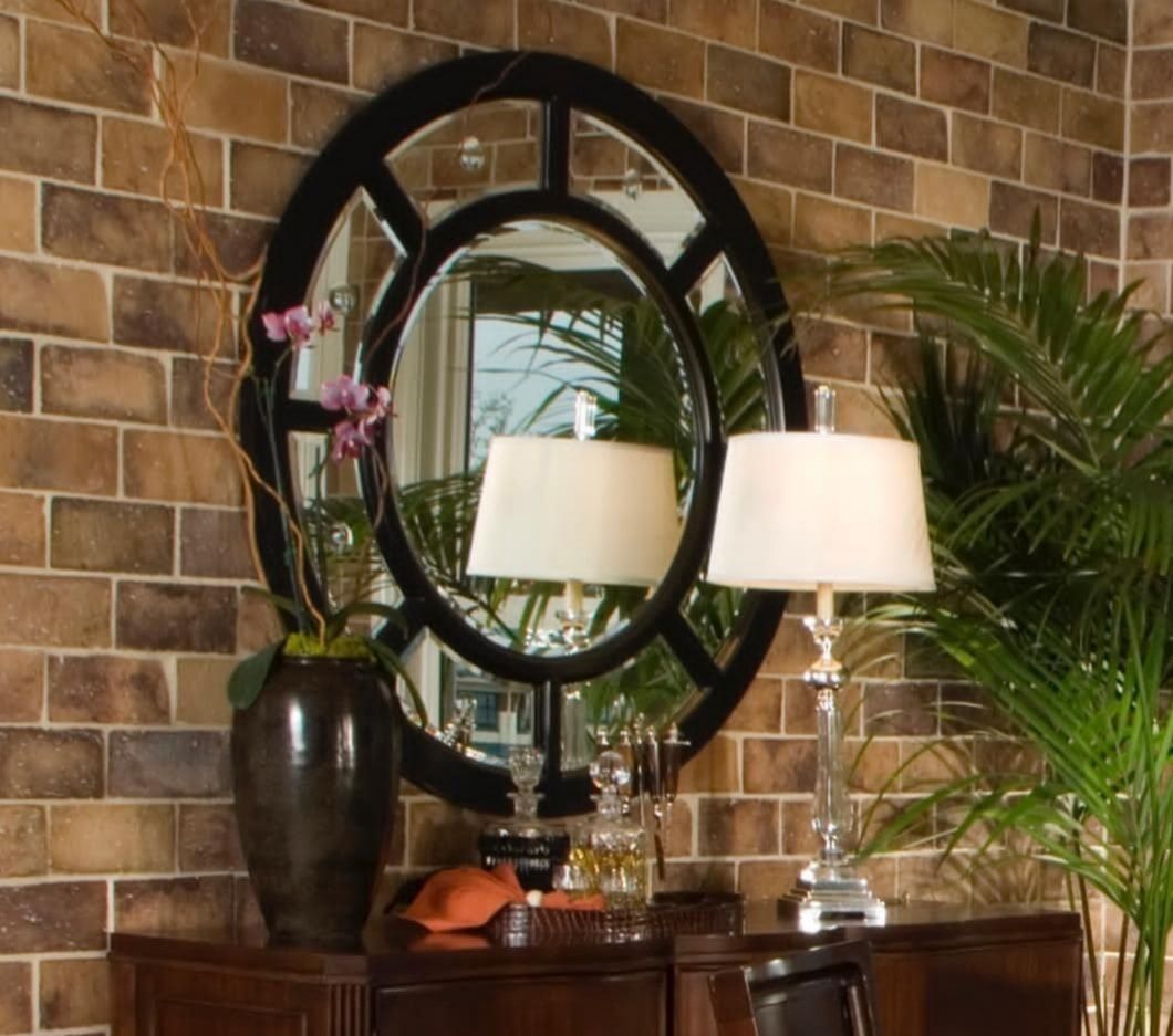 Mirror and lamp on a wooden dresser against a brick wall, with a vase and potted palm nearby