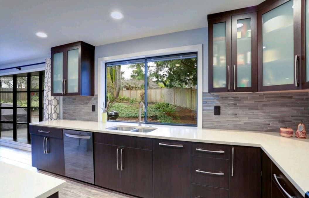 Modern kitchen with dark cabinets, white countertops, and a large window overlooking a garden