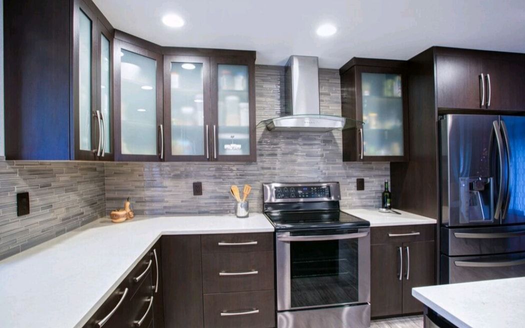 Modern kitchen with dark cabinets, stainless steel stove, glass-front uppers, and gray tile backsplash