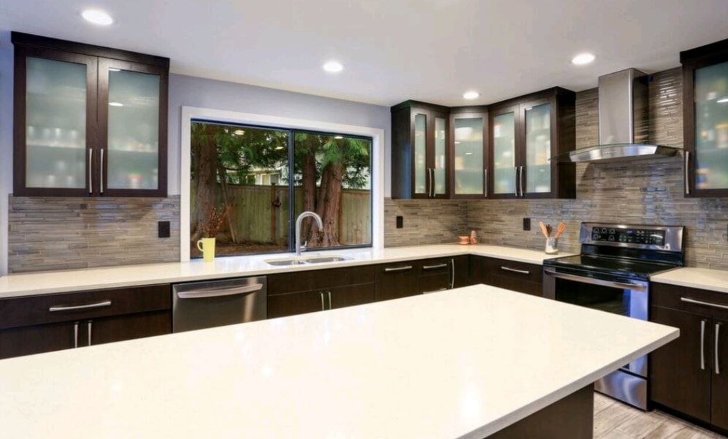 Modern kitchen with white island, dark cabinets, stainless appliances, and a large window above the sink