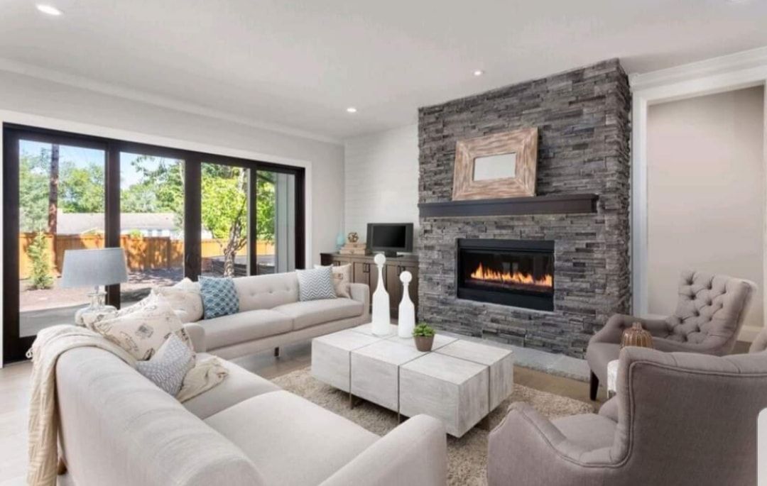 Modern living room with stone fireplace, white sofas, and large windows overlooking greenery