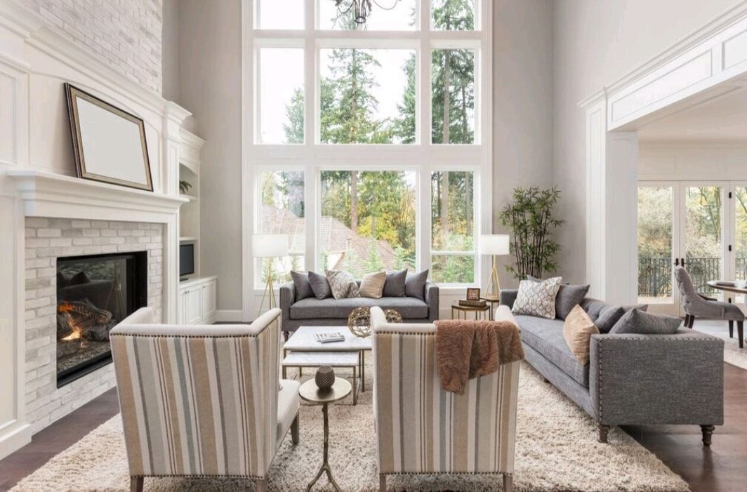 Bright living room with fireplace, large windows, gray sofas, and striped armchairs around a coffee table