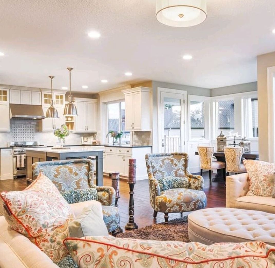 Bright open kitchen and living area with patterned chairs, white cabinets, and soft neutral decor