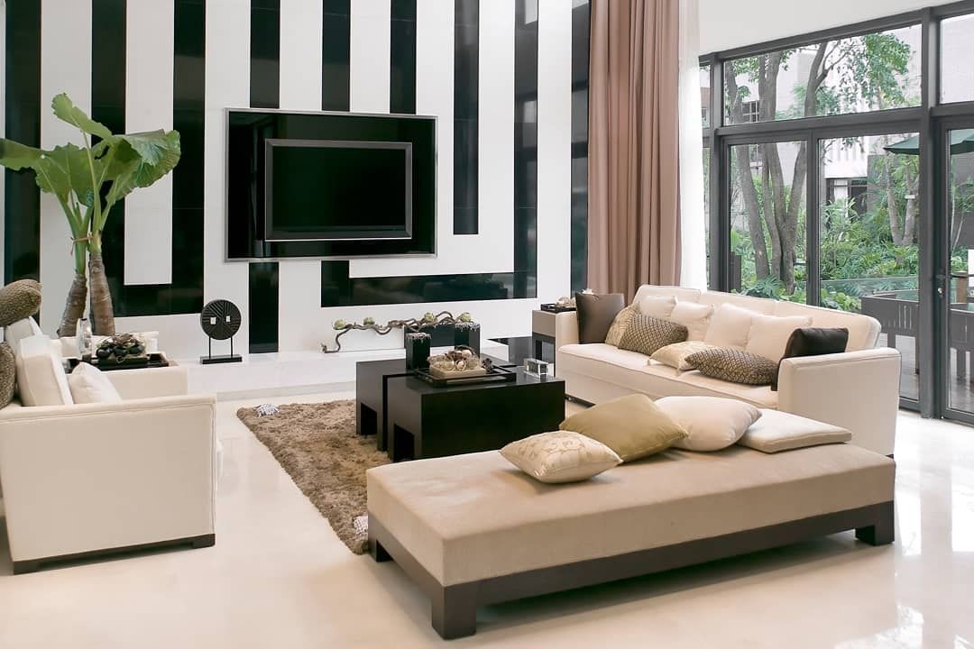 Modern living room with white and beige sofas, black TV, striped wall, and large windows.