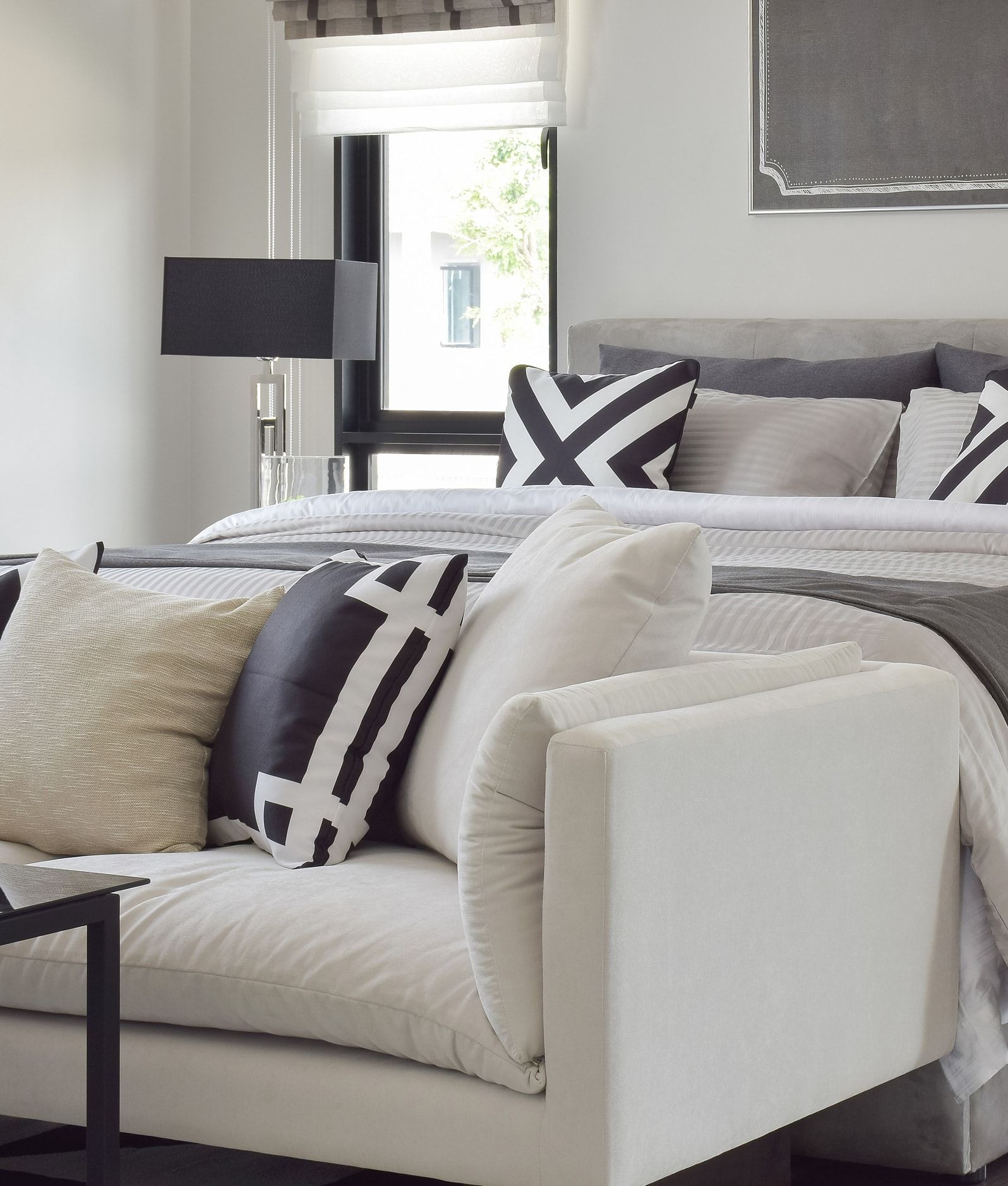 Stylish bedroom with a white sofa, gray bedding, black lamp, and black-and-white pillows.
