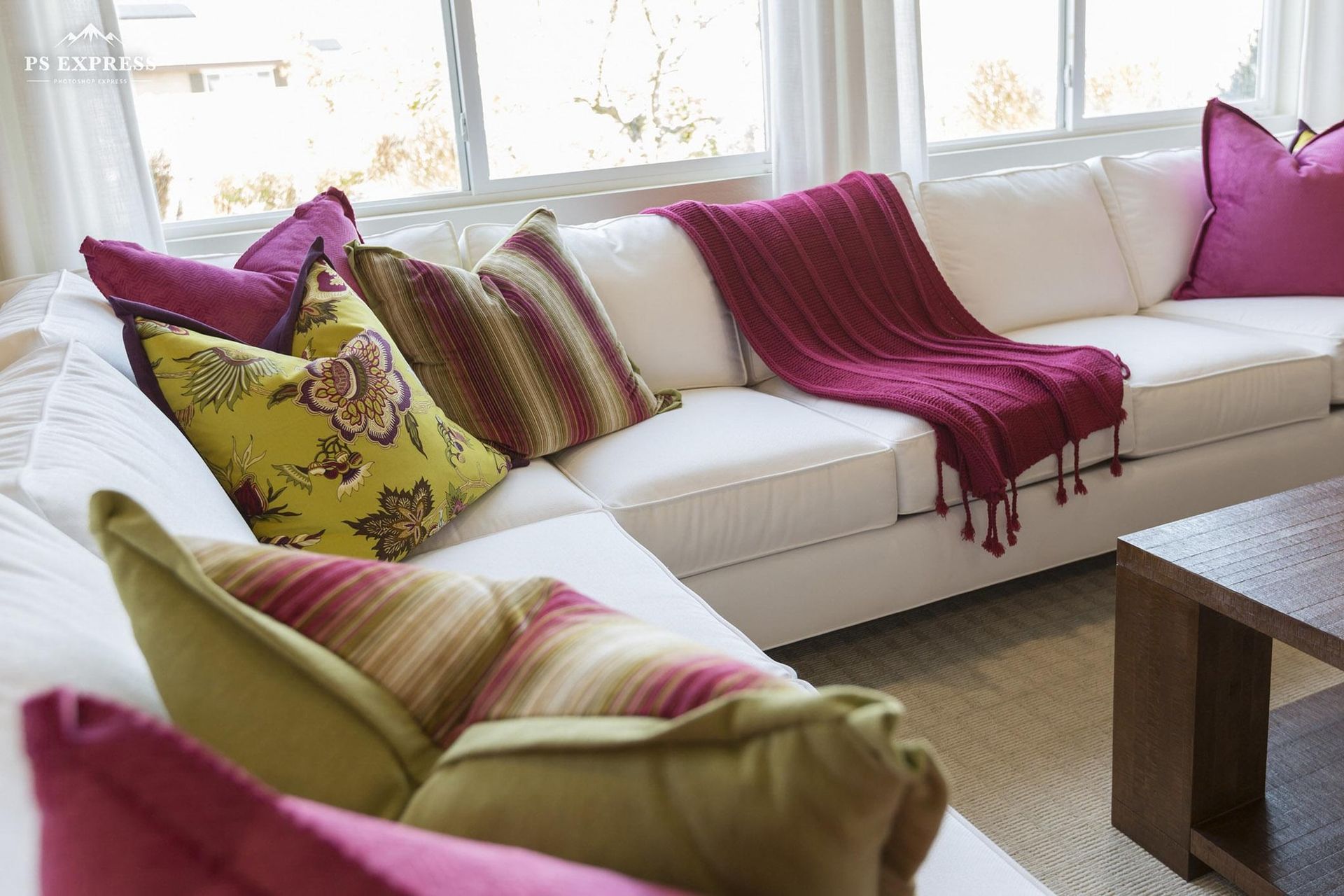 Bright living room with white sofa, magenta throw and pillows near a window, plus a wooden coffee table.