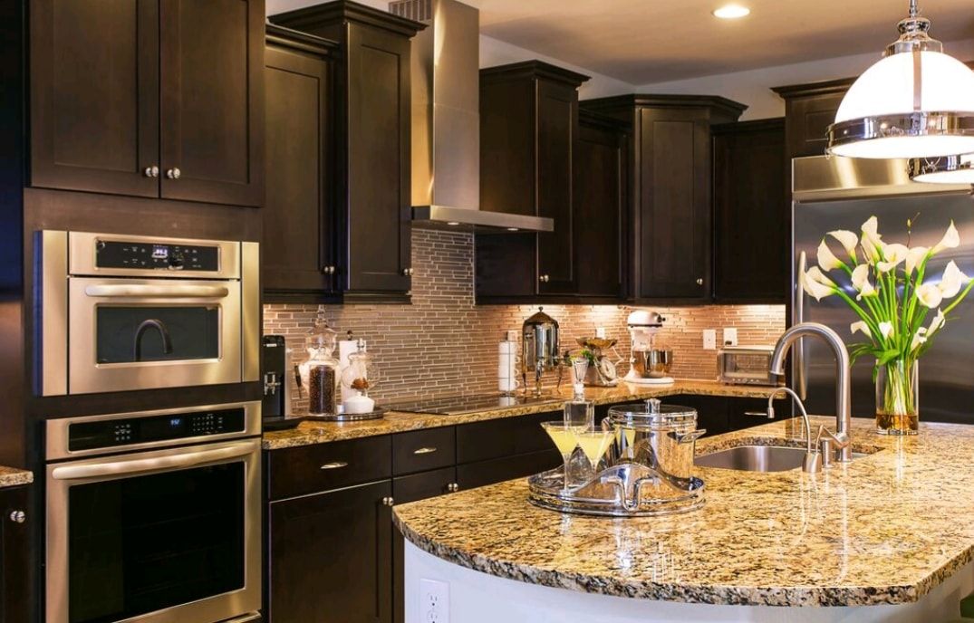 Modern kitchen with dark cabinets, granite island, stainless appliances, and a vase of flowers