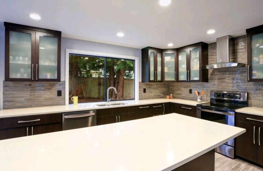 Modern kitchen with white island, dark cabinets, stainless appliances, and large window above the sink