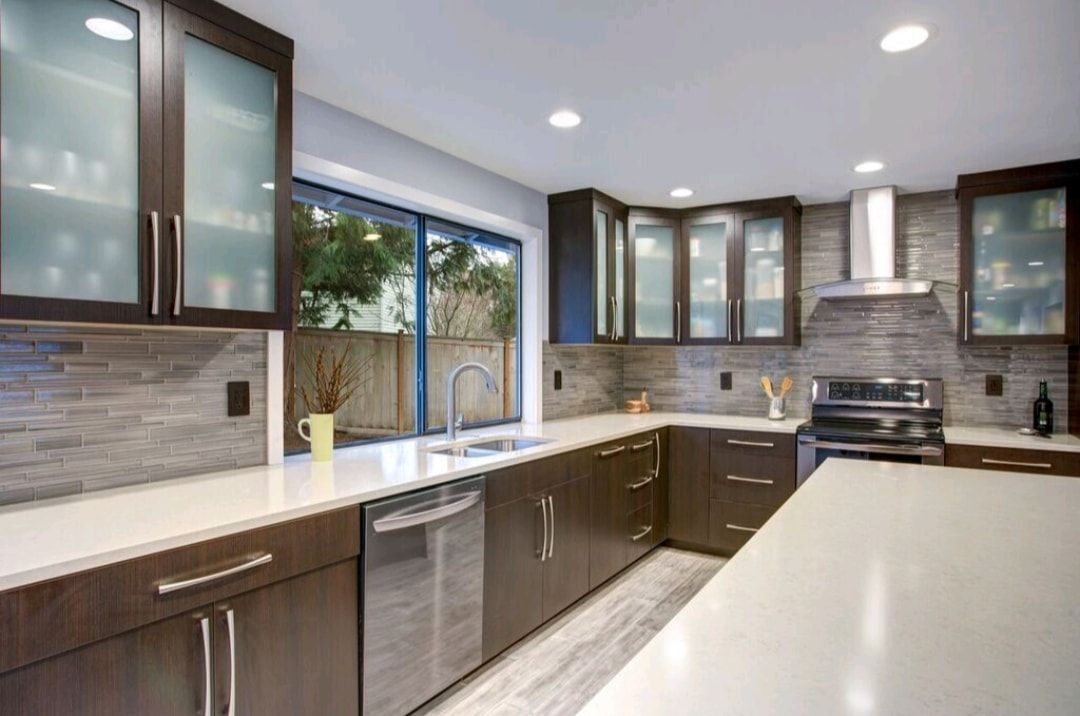 Modern kitchen with dark wood cabinets, stainless appliances, large window, and white countertops