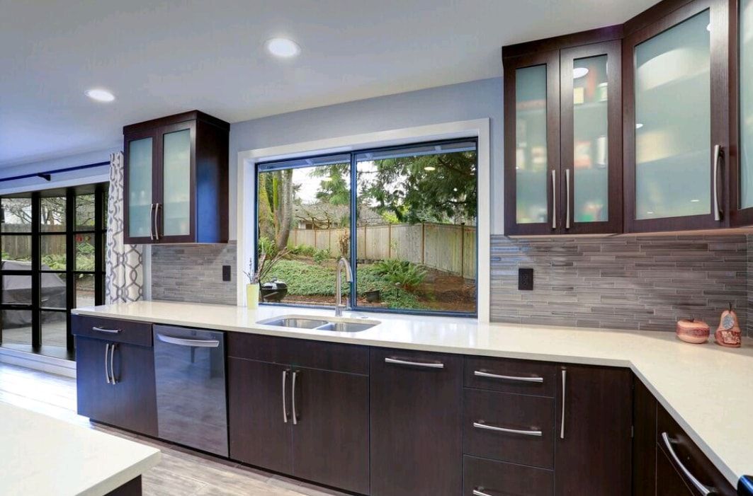 Modern kitchen with dark wood cabinets, light countertops, and a large window above the sink