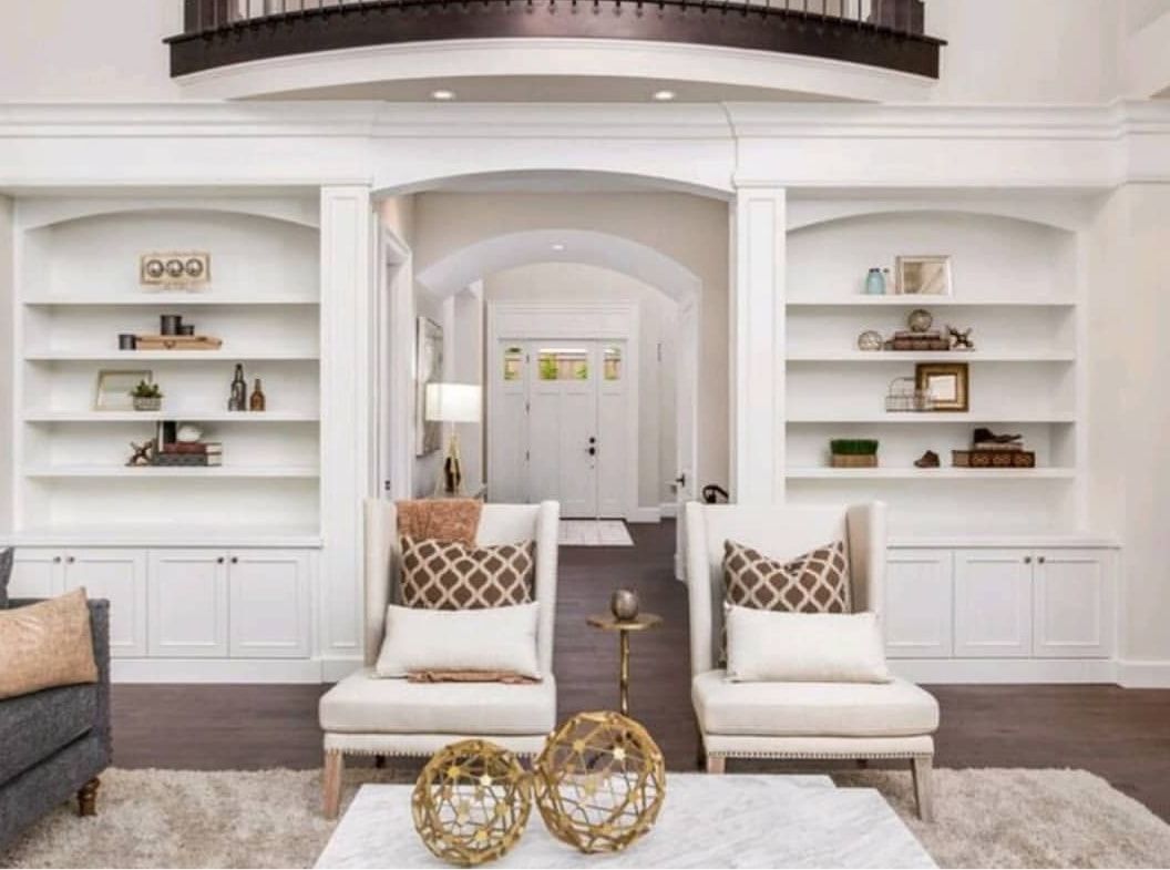 Bright white living room with built-in shelves, two cream chairs, and gold decor accents