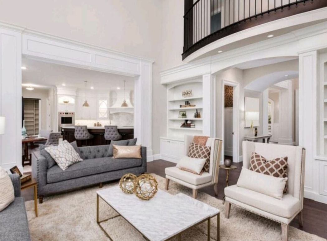Bright open living room with gray sofa, two white chairs, marble coffee table, and curved balcony above