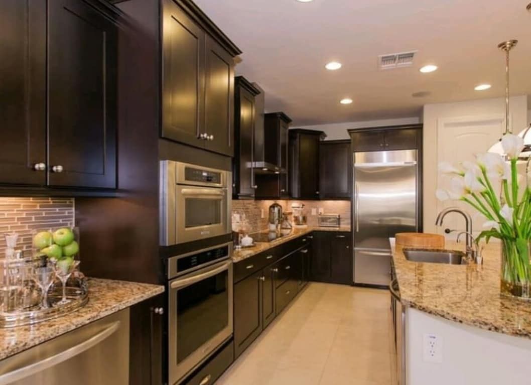 Modern kitchen with dark cabinets, granite countertops, stainless steel appliances, and tiled floor