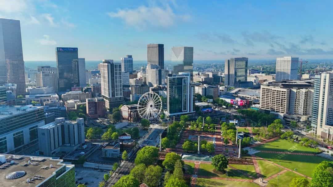 Aerial view of a city skyline with a ferris wheel, parks, and modern buildings under a blue sky.