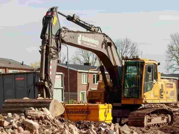 Yellow excavator at a construction site, lifting rubble beside houses