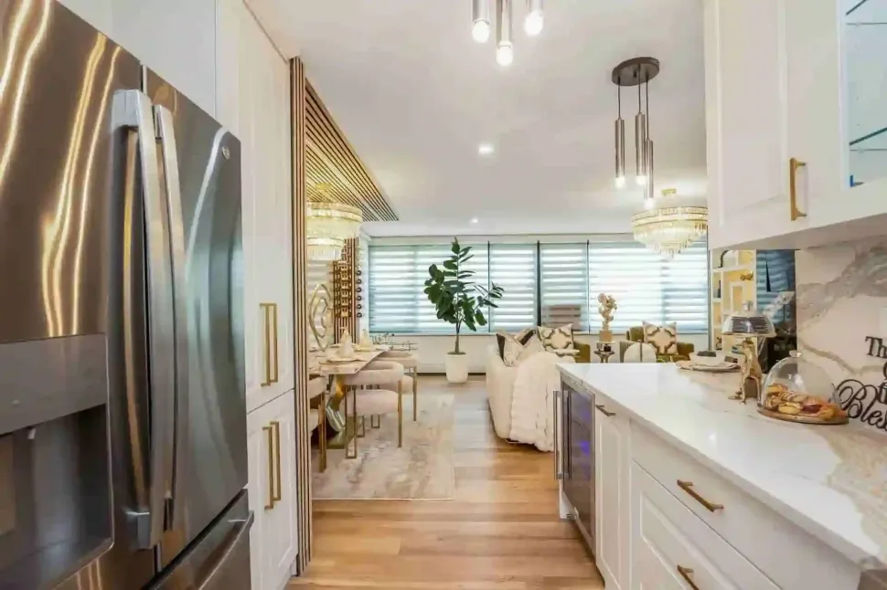 Bright modern kitchen with white cabinets, stainless fridge, wood floors, dining area by the window