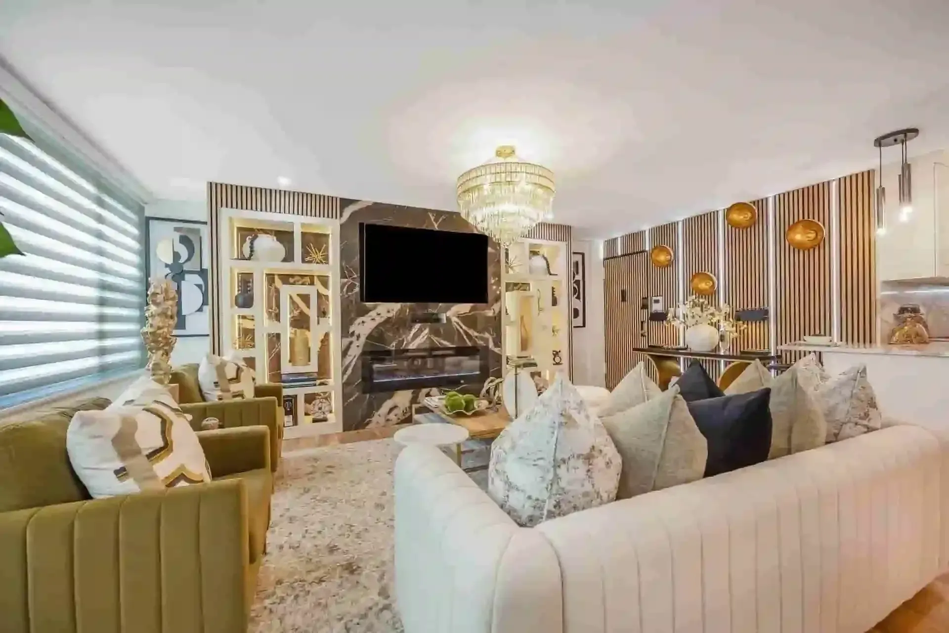modern living room with cream sofas, gold accents, chandelier, large TV above a fireplace
