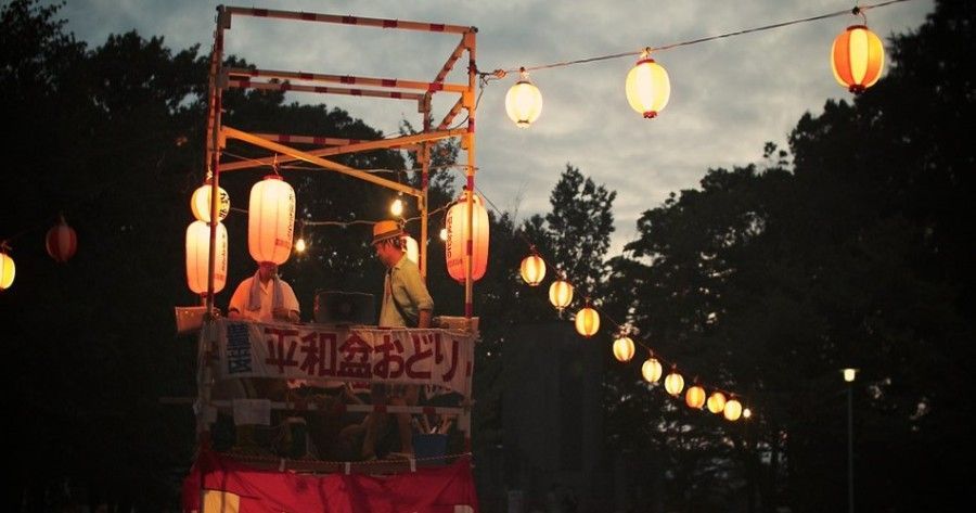 Lantern-lit festival float with Japanese banners at dusk, glowing against a dark tree-lined sky