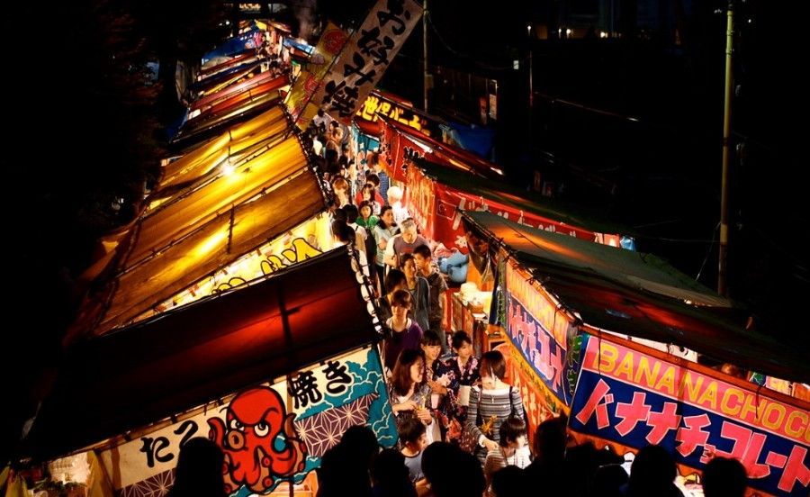 Night market alley packed with glowing stalls and crowds beneath colorful Japanese signs