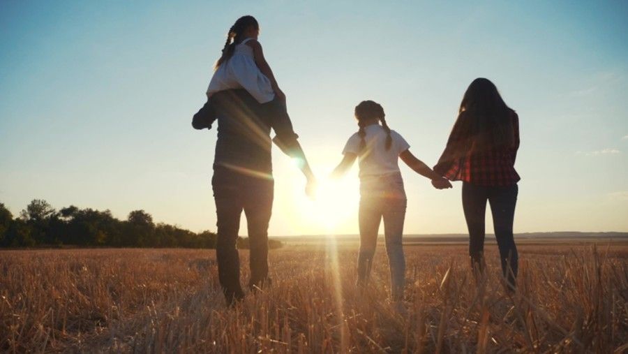 A family is walking through a wheat field at sunset holding hands.