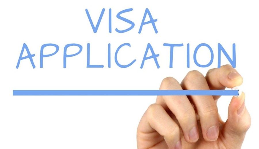A person is writing the word visa application with a marker