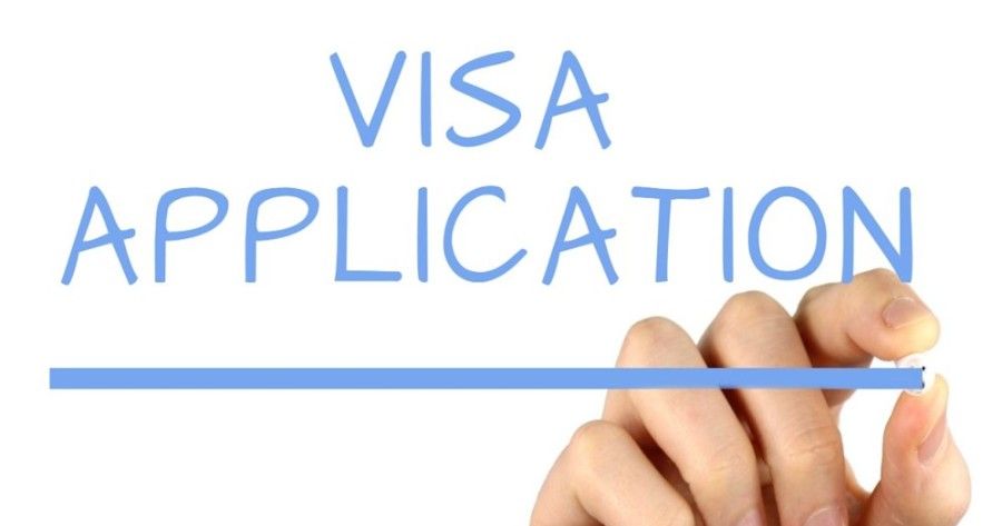 A person is writing the word visa application with a marker.