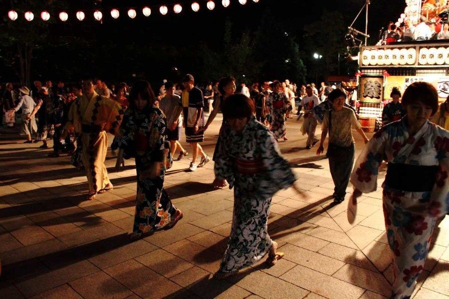 People in colorful yukatas dancing at a nighttime festival under string lights