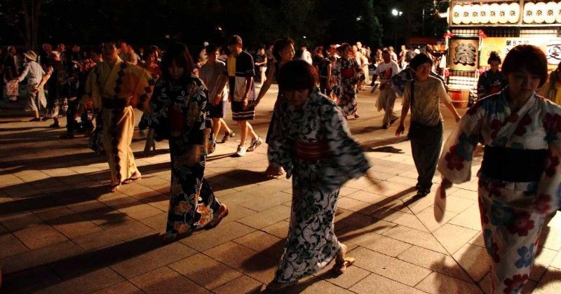 People in colorful kimono walking at a nighttime street festival with lantern-lit stalls