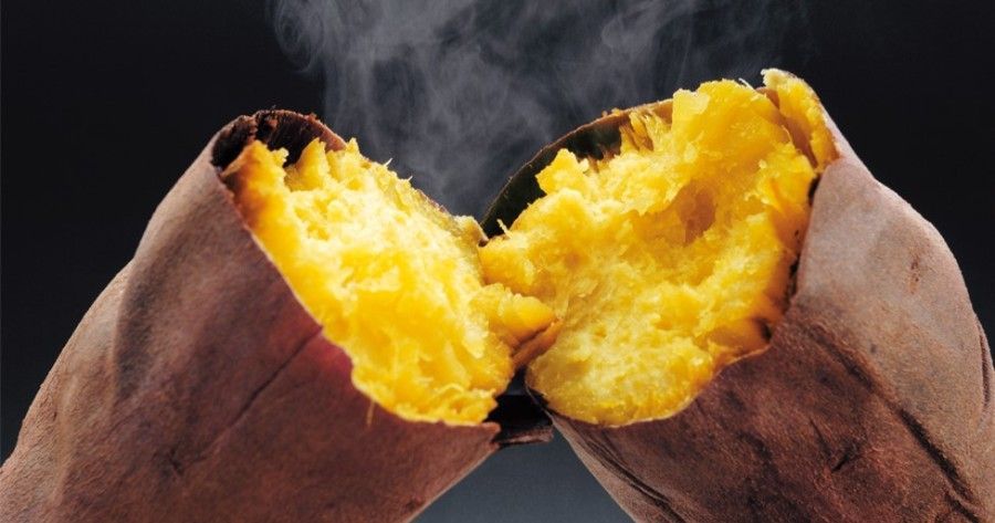 Two hands holding open a baked sweet potato with bright orange flesh