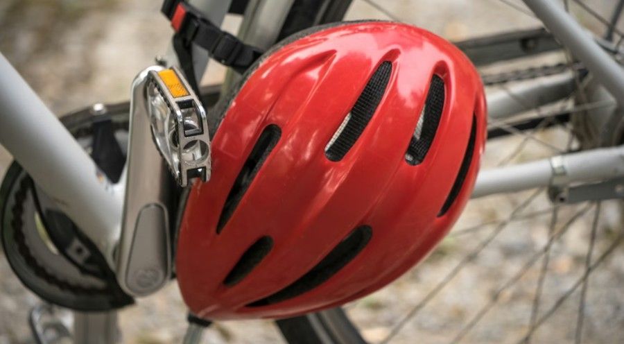Red bicycle helmet clipped to a bike frame, with blurred wheels in the background