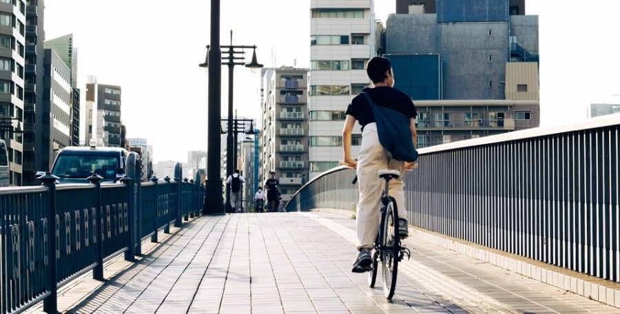Cyclist riding on a city bridge walkway with buildings and traffic in the background