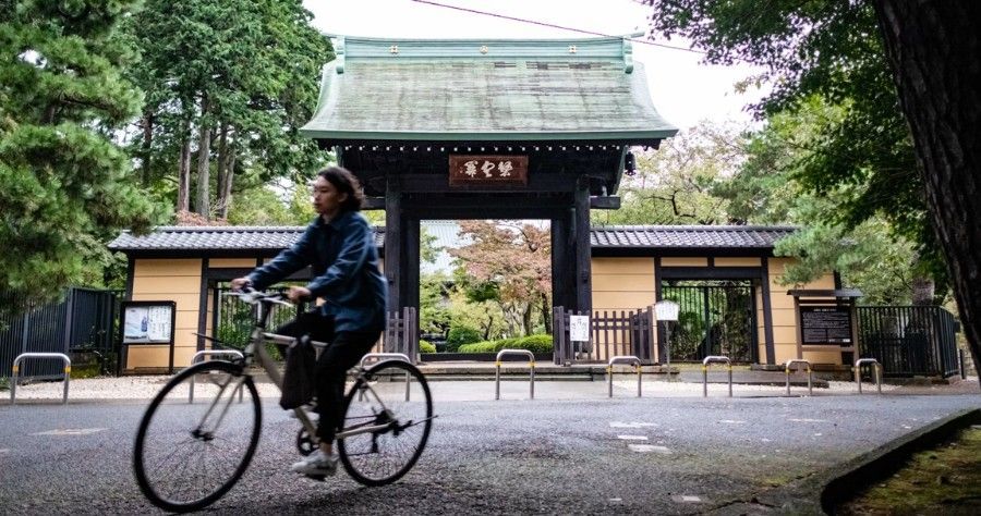 Cyclist riding past a traditional temple gate framed by trees and gravel path