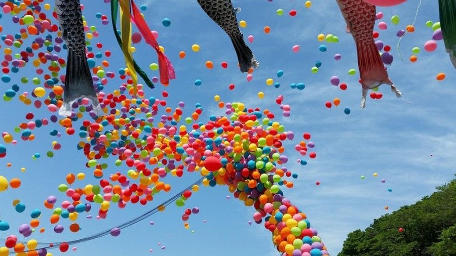 A bunch of colorful balloons are flying in the sky with Japanese Carp streamers at the top