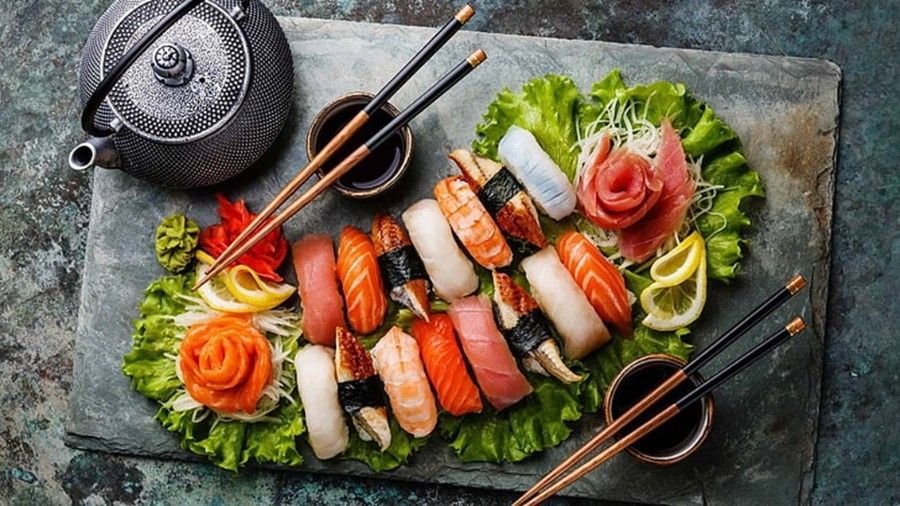 A plate of sushi with chopsticks and a teapot on a table.