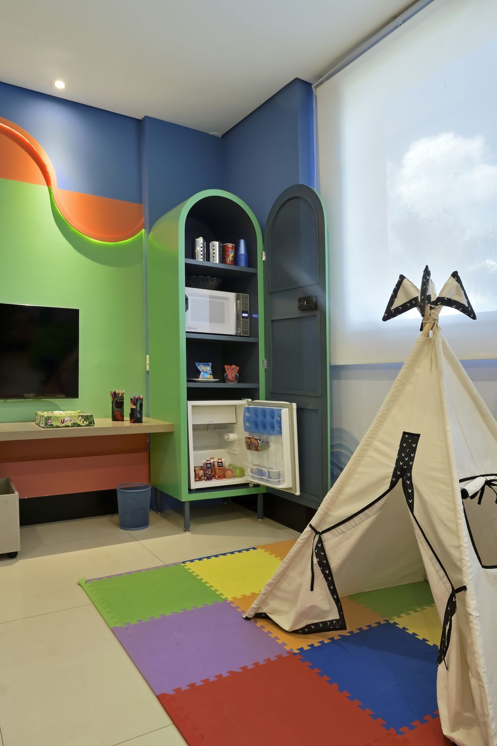 Uma sala com muitos brinquedos, mesas e cadeiras.
